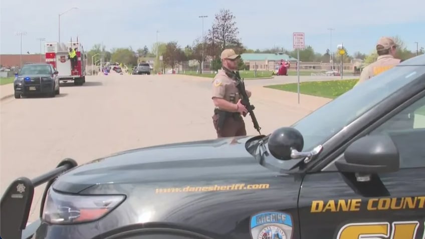 An officer stands outside the school with a rifle