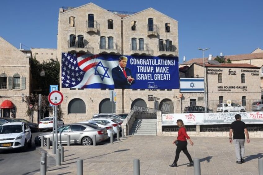 People in Jerusalem walk past a billboard congratulating US President-elect Donald Trump o