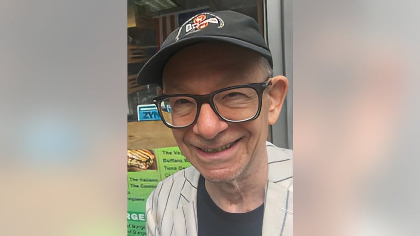 A close-up of John Meyer smiling wearing glasses and a hat