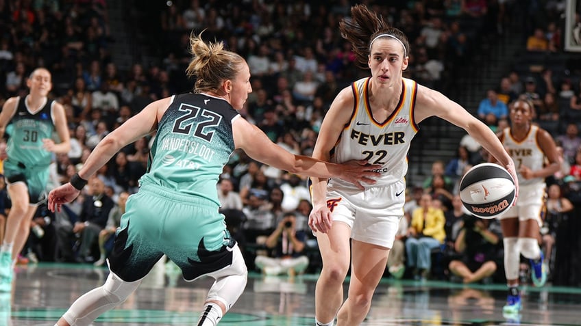 Caitlin Clark dribbles around a player