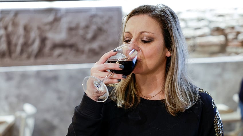 A blonde woman drinks red wine from a glass.