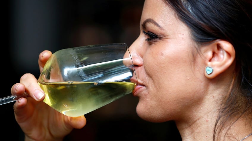 A woman drinks white wine from a glass.