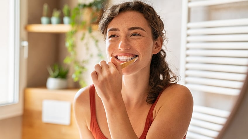 Smiling woman brushing teeth in bathroom