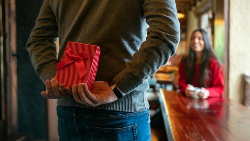 Man holds a Valentine's Day gift behind his back