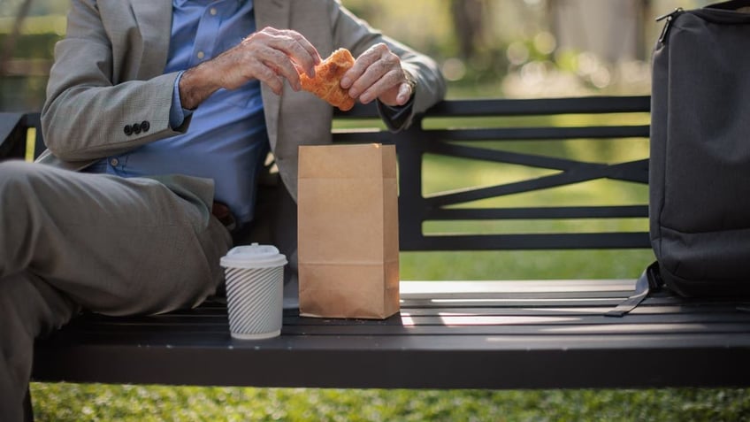 Close-up of man eating croissant on bench