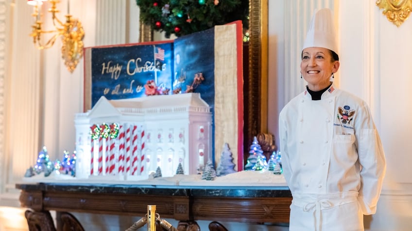 The White House executive pastry chef standing next to gingerbread house