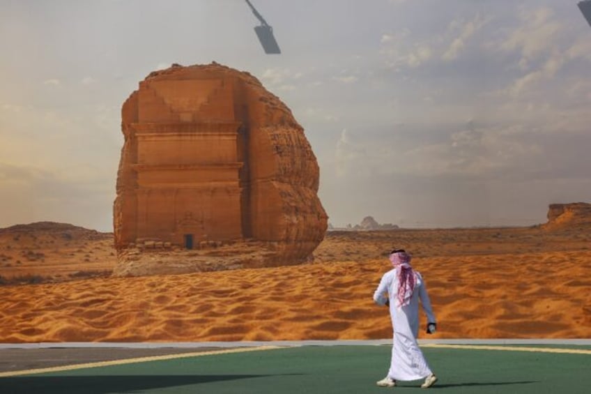 A COP16 delegate walks past a giant poster of a Saudi archaeological site at the start of