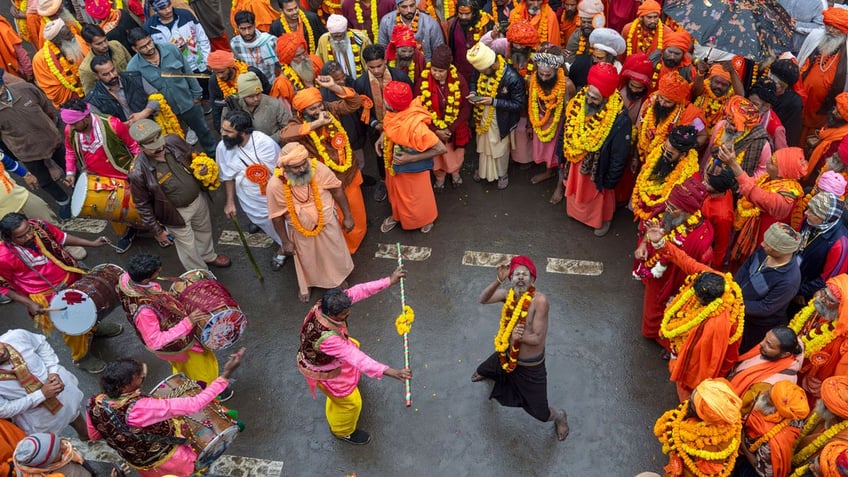 A crowd of Hindu worshippers dressed in orange, yellow and pink gather around an ascetic dancer.