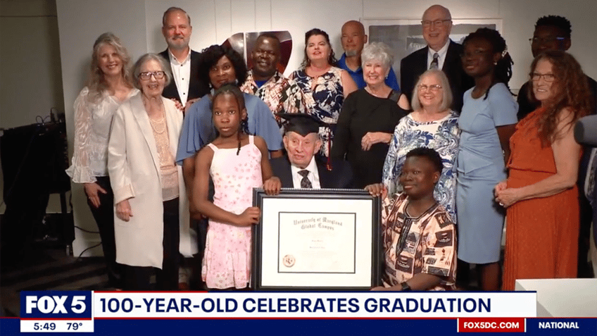 man seated, holding a diploma, surrounded by family