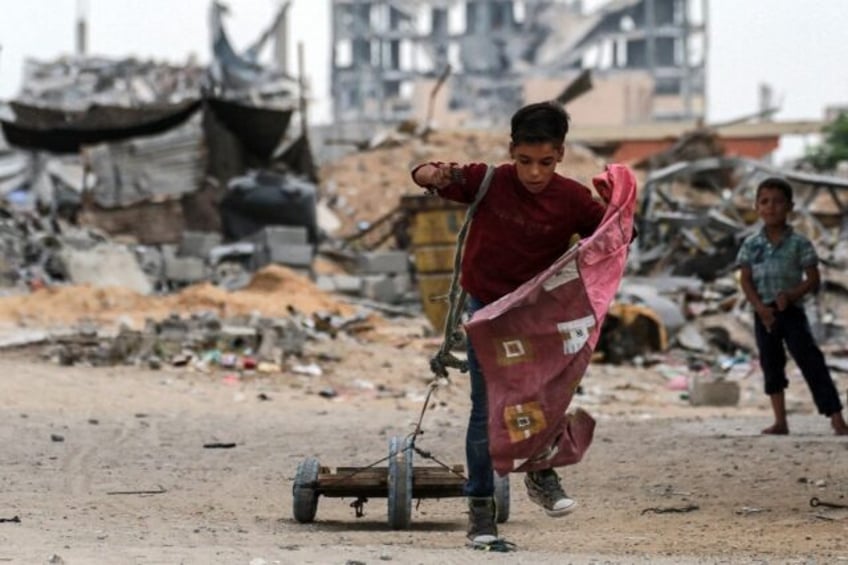 A boy pulls a cart with a rope while walking past a destroyed building in Khan Yunis in th