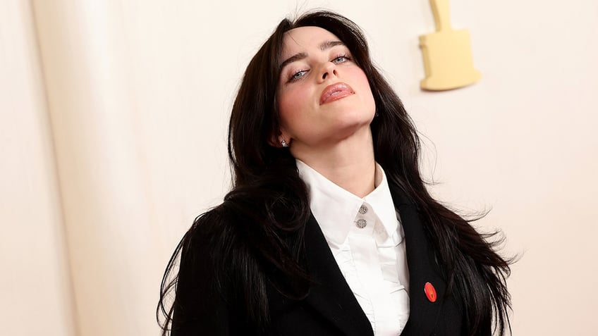 Billie Eilish tilts her head up on the carpet wearing a black suit at the Academy Awards