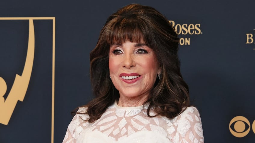 Kate Linder smiles and looks to her right at the Daytime Emmy Awards wearing a white dress with a transparent neckline